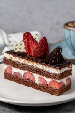 Koyu arkaplanda çilekli ve çikolatalı pasta. Katmanlı çikolatalı kek ve kahve fincanı. Pasta ürünleri. Kapat.