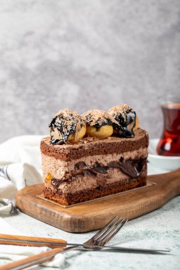 Chocolate and profiteroles cake. Layered cake with chocolate and cream on a wooden serving board on a stone background. close up