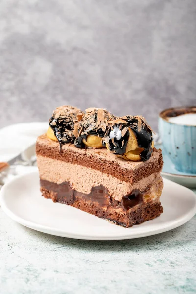 Chocolate and profiteroles cake. Layered cake with chocolate and cream on plate on stone background. close up