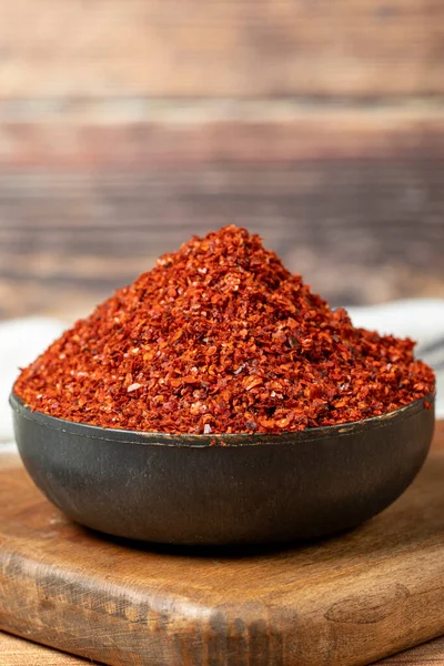Red pepper flakes. Crushed chili pepper in bowl, dried chili flakes on wooden background. Close up