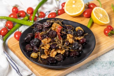 Mixed black olives. Special mixed olives prepared with dried red pepper, sun-dried tomatoes, thyme, walnuts and rosemary on a wooden serving plate. close up