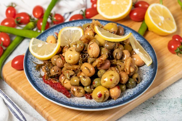 Special mixed olives prepared with green olives, dried red peppers, sun-dried tomatoes, thyme, walnuts and rosemary. Mixed olives with special sauce on a wooden serving plate. close up