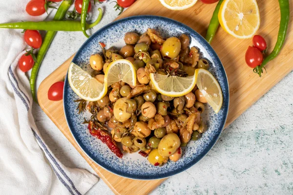 Special mixed olives prepared with green olives, dried red peppers, sun-dried tomatoes, thyme, walnuts and rosemary. Mixed olives with special sauce on a wooden serving plate. Top view