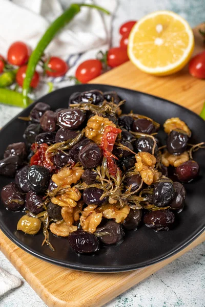 Mixed black olives. Special mixed olives prepared with dried red pepper, sun-dried tomatoes, thyme, walnuts and rosemary on a wooden serving plate. close up