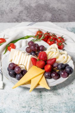 Cold cheese plate, cheese set platter. Strawberry, grape and cheese assortment on gray background