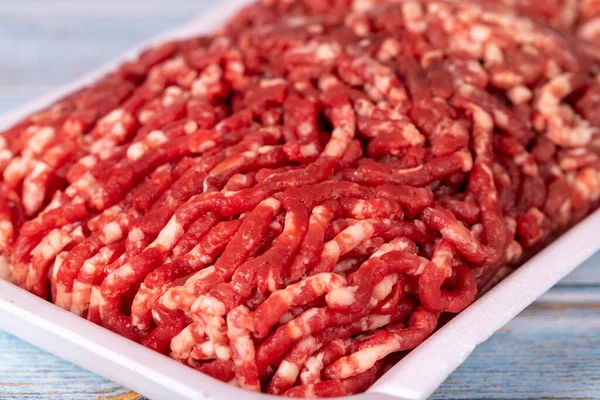 Raw ground beef in a white polystyrene tray on a wood background. Fresh ground beef on wood background. Close up