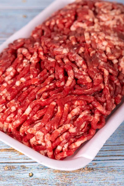 Raw ground beef in a white polystyrene tray on a wood background. Fresh ground beef on wood background. Close up