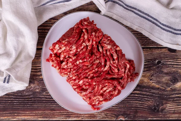 Beef minced on the plate. Fresh ground beef on wood background. Top view