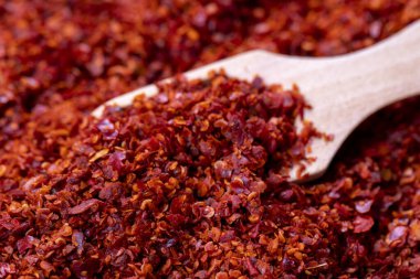 Çekirdeksiz kırmızı biberli gevrek. Arka planda tahta kaşıkla kurutulmuş kırmızı biber taneleri var. Baharatlar ve bitkiler. Kapat.