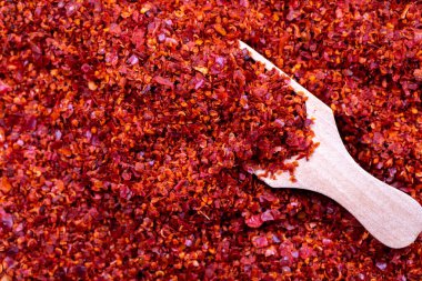 Çekirdeksiz kırmızı biberli gevrek. Arka planda tahta kaşıkla kurutulmuş kırmızı biber taneleri var. Baharatlar ve bitkiler. Metin için boş alan. Kapat.