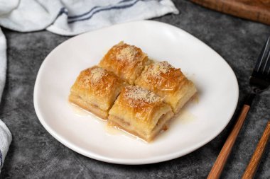 Sütlü ve fındıklı baklava. Türk mutfağı lezzetleri. Siyah arka planda süt olan baklava. Yerel adı Sutlu Nuriye. Kapat.