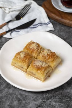 Sütlü ve fındıklı baklava. Türk mutfağı lezzetleri. Siyah arka planda süt olan baklava. Yerel adı Sutlu Nuriye. Kapat.