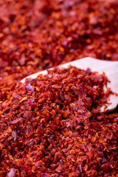 Chilli pepper seedless flakes. Heap of dried red pepper flakes with wooden spoon as background. Spices and herbs. Close up