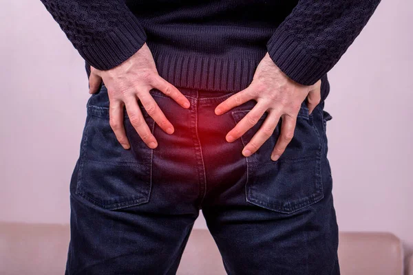 Man with diarrhea problem, man with digestive problem touching his buttock, man with hemorrhoid problem on grey background. Painful area highlighted in red