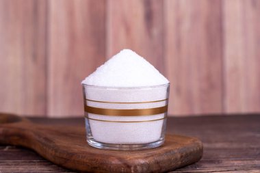 Granüle şeker. Tahta zemin üzerinde cam kasede beyaz granüllü şeker.