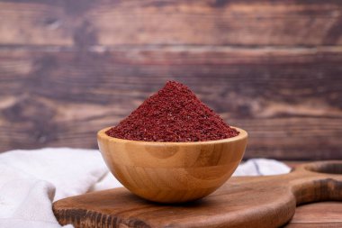 Sumac on wooden background. Dried ground red Sumac powder spices in wooden bowl clipart