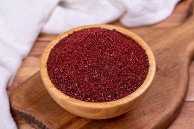 Tahta arka planda Sumac. Kurumuş toprak, kırmızı Sumac tozu, ahşap kasede baharatlar.
