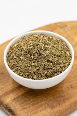 Beyaz arka planda izole edilmiş kuru ezilmiş fesleğen. Seramik kasede kurutulmuş fesleğen tozu baharatları. Baharat konsepti. Kapat.