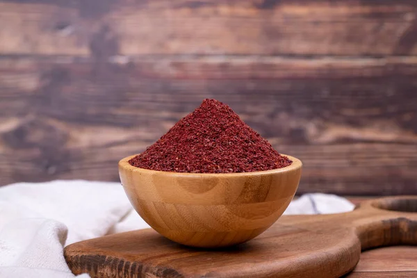 Tahta arka planda Sumac. Kurumuş toprak, kırmızı Sumac tozu, ahşap kasede baharatlar.