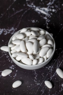 Badem şekeri. Şeker kaplı badem şekeri koyu arkaplanda seramik kasede. Çok renkli küçük şekerler. Kapat.