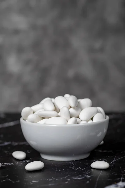 Almond candy. Sugar coated almond candy in ceramic bowl on dark background. Small multi-colored candies