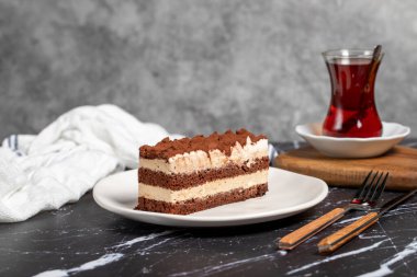 Geleneksel İtalyan tatlı tiramisu keki. Bir dilim çikolatalı pasta, tiramisu kreması ve koyu masa üzerine kakao tozu..