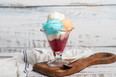 Dondurma ahşap arka planda. Cam kasede karışık dondurma topları. Dondurma kabında kiraz, limon, karamel, çikolata ve süt dondurması. Kapat.