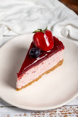 Meyveli kek dilimi. Ahşap arka planda böğürtlen soslu cheesecake dilimi