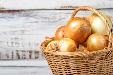 Fresh raw onion in a basket over wooden background. Onion harvest season concept. Vegetables for a healthy diet. Copy space. Empty space for text