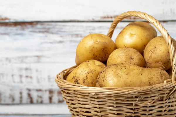 Fresh raw potato in a basket over wooden background. Potato harvest season concept. Vegetables for a healthy diet. Copy space. Empty space for text