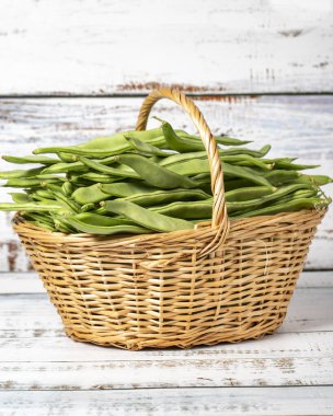 Hasır sepetteki taze yeşil fasulyeler ahşap arka planda. Fasulye hasat mevsimi konsepti. Sağlıklı bir diyet için sebzeler. Kapat.