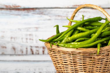 Hasır sepette taze yeşil biber, ahşap arka planda. Yeşil biber hasat mevsimi konsepti. Sağlıklı bir diyet için sebzeler. Uzayı kopyala Metin için boş boşluk