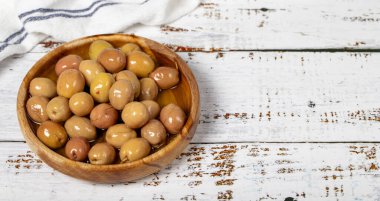 Ahşap kasede çizilmiş yeşil zeytin. Beyaz ahşap arka planda yeşil zeytin. Akdeniz yemekleri. Vejetaryen yemeği. Uzayı kopyala Metin için boş boşluk