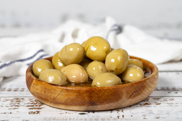 Green olives at wooden bowl. Olives on a white wood background. Mediterranean food. vegan food