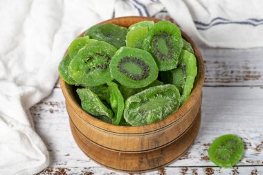 Tahta kasede kurutulmuş kivi dilimleri. Beyaz ahşap arka planda güneşte kurutulmuş kivi dilimleri. Kapat.