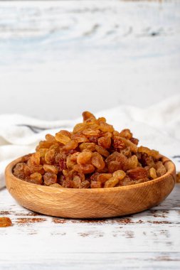 Kuru üzümler ahşap kasede. Beyaz ahşap arka planda güneşte kurutulmuş doğal kuru üzümler. Kapat.