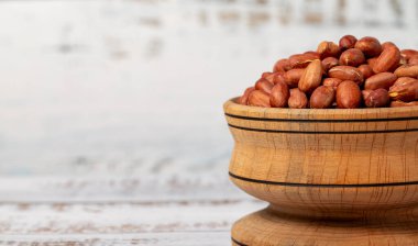 Tahta kasede yer fıstığı. Beyaz ahşap arka planda kabuklu fıstıklar. Uzayı kopyala Metin için boş boşluk