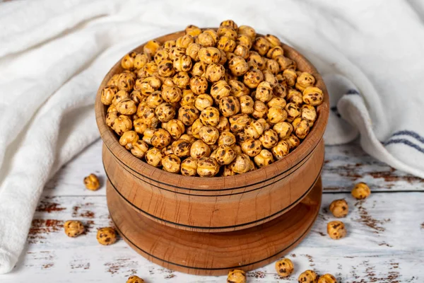 Roasted chickpeas in a wood bowl. Chickpeas on white wood background. Close up
