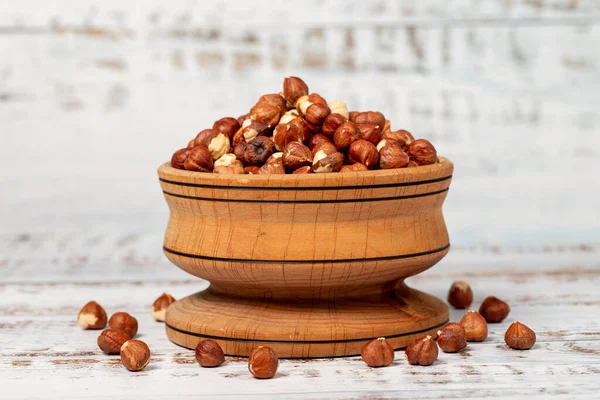 Hazelnuts in wood bowl. Peeled hazelnuts kernel on white wood background