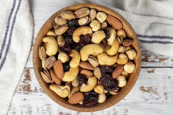 Mixed nuts in wood bowl. Nuts on white wood background. Mixed nuts prepared with hazelnuts, almonds, cashews, pistachios, pistachios and grapes. Top view