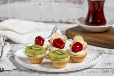 Meyveli turtalar. Bir tabakta çilek, muz ve kivili tart. Atıştırmalık tatlı yemek. Kapat.