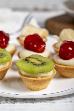 Meyveli turtalar. Bir tabakta çilek, muz ve kivili tart. Atıştırmalık tatlı yemek. Kapat.