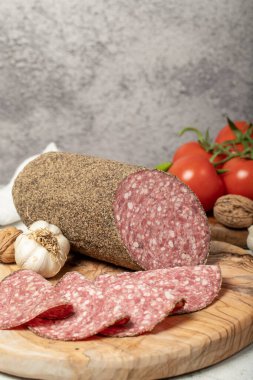 Biberli salam ve kesme tahtasında dilimler. Gri arka planda biberli İtalyan salamı. Kapat.