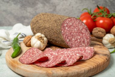 Biberli salam ve kesme tahtasında dilimler. Gri arka planda biberli İtalyan salamı. Kapat.