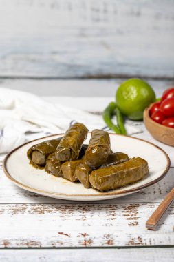Zeytin yağıyla doldurulmuş üzüm yaprakları. Üzüm yaprakları ve pirinç ile hazırlanmış Dolma. Doldurulmuş üzüm yaprakları ya da beyaz ahşap arka planda zeytin yağı ile dolmades. Yerel adı Yaprak Sarma. Kapat.