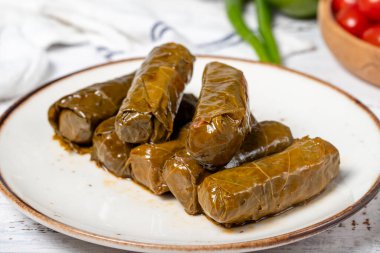 Zeytin yağıyla doldurulmuş üzüm yaprakları. Üzüm yaprakları ve pirinç ile hazırlanmış Dolma. Doldurulmuş üzüm yaprakları ya da beyaz ahşap arka planda zeytin yağı ile dolmades. Yerel adı Yaprak Sarma. Kapat.