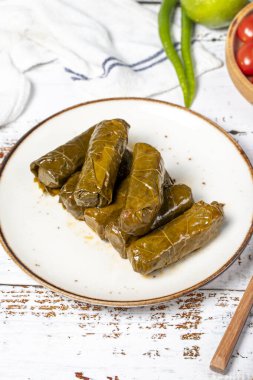 Zeytin yağıyla doldurulmuş üzüm yaprakları. Üzüm yaprakları ve pirinç ile hazırlanmış Dolma. Doldurulmuş üzüm yaprakları ya da beyaz ahşap arka planda zeytin yağı ile dolmades. yerel adı yaprak sarma
