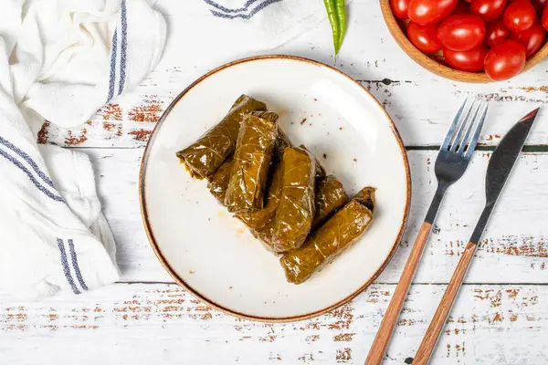 Stuffed grape leaves with olive oil. Dolma prepared with grape leaves and rice. Stuffed grape leaves or dolmades with olive oil on a white wooden background. local name yaprak sarma. Top view