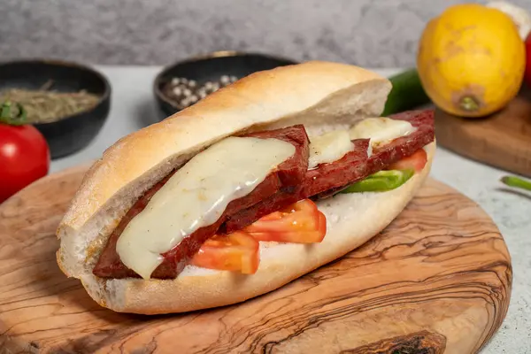 Turkish bread sandwich with kashar sausage on the presentation board. Sausage in bread prepared with tomatoes, peppers and meatballs. Local name ekmek arasi sucuk