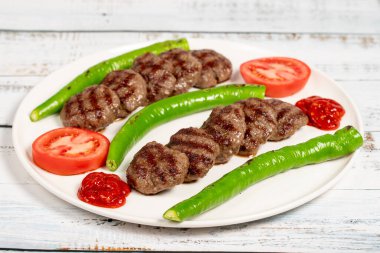 Izgara köfte. Ahşap zemin üzerinde kavrulmuş biber ve domatesli Türk köfteleri.